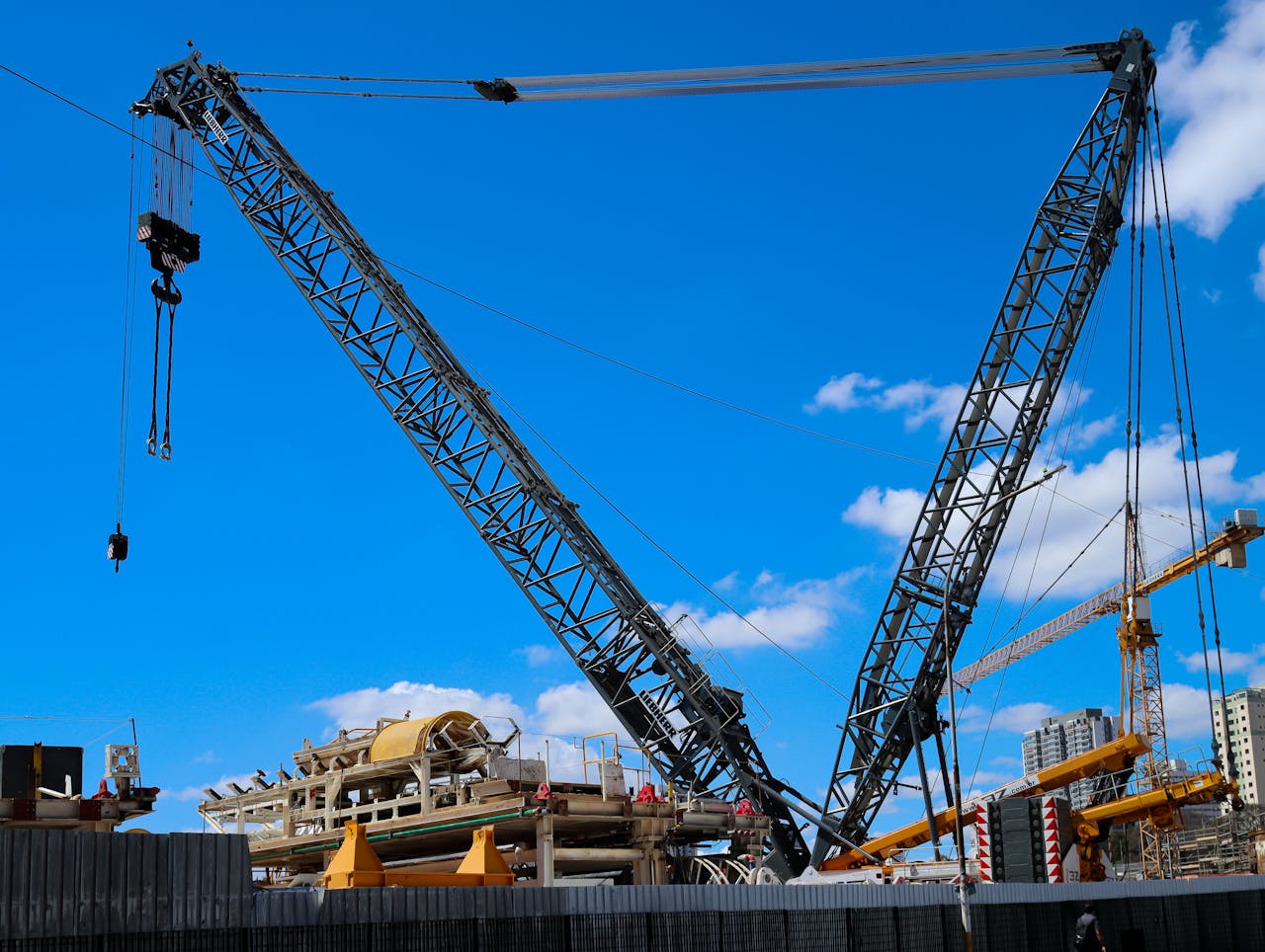 about-us-01 Large tower cranes dominate a construction site under a bright blue sky, symbolizing urban development.